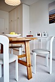 White chairs with upholstered seats around wooden table in in bright dining room