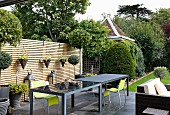 Elegant, grey outdoor tables and neon-green chairs on terrace in front of slatted wooden screen