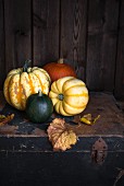 Various pumpkins with autumnal leaves on an old wooden chest