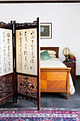 Carved screen with Asian characters in front of an antique bed