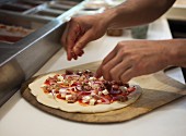 A pizza baker placing toppings on a pizza