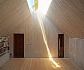 Raum mit Holzverkleidung und Oberlichtband in Dachschräge, strahlende Lichtreflexion auf Dielenboden