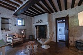 Fireplace in living room with tiles floor, whitewashed stone walls and rustic wood-beamed ceiling