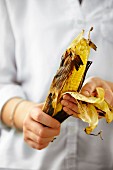 A woman peeling a grilled corn cob