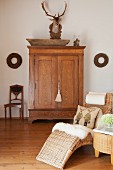 Sheepskin and scatter cushions on comfortable wicker chaise longue in front of hunting trophy above oak cabinet