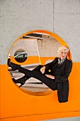 An older business woman sitting in a circle cut into a wall