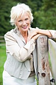 An older woman leaning on a wooden fence