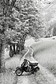 Motorroller steht auf Feldweg in Berglandschaft (s/w-Foto)