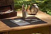 Pen holder covered in map and old alarm clock on wooden table outdoors