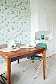 Kitchen table and vintage folding chair in front of bird-patterned wallpaper