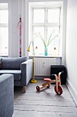 Retro wooden tricycle and yellow standard lamp in front of window in corner of living room with rustic wooden floor