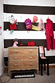 Colourful children's accessories hung from coat pegs and vintage chest of drawers against wall decorated in wide black and white stripes