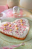 A heart-shaped cake decorated with pink sugar hearts under a glass cloche