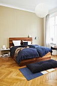 Edles Holzbett mit blauer Bettwäsche in Schlafzimmer mit Fischgrätparkett