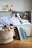 Kinderbett mit hellgrauer Holzverkleidung, Bettschublade und Kuscheltieren