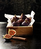 Fresh figs in a wooden crate with paper with a halved fig and a knife in the foreground