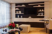 Fitted cabinets with integrated flatscreen TV in classic, elegant interior with velvet-covered pouffes