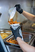 Sweet potato chips being transferred into a newspaper cone