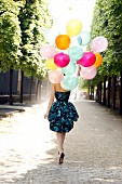Junge Frau in Cocktailkleid mit vielen Luftballons