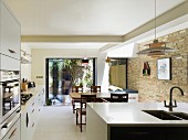 Open-plan, modern kitchen with traditional dining area, old brick wall and view of summer terrace seating area