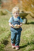 A little girl holding a bowl of eggs in a field