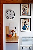 Framed Japanese artworks next to clock on kitchen wall