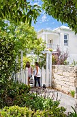 Two women with a dog at a white-painted garden gate in front of an elegant country house