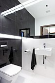 Designer bathroom with white floor tiles, black wall tiles and mirrored wall above sink