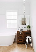 Vintage vanity furniture made of rustic wood in the corner of a bathroom next to a free-standing white bathtub