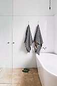 Freistehende Badewanne in bodenebenem Duschbereich mit schwarz-weiß gestreiften Handtüchern an weiß gefliester Wand