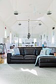 Black leather couch in open, former church room under pendant lights, dining area in background