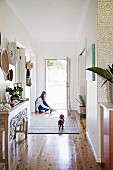 Entrance area with shiny floorboards, in the background girl in front of an open door with a dachshund on a carpet runner