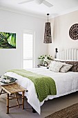 Double bed with upholstered headboard and green bedspread, bamboo bench at the end of the bed