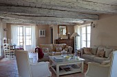 Helle, antike Sessel und Sofagarnitur in offenen Wohnbereich eines provenzalischen Landhaus mit weiß getünchter Holzbalkendecke