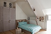 Doppelbett mit karierter Bettwäsche unter Dachschräge, grauer Einbauschrank mit Lamellentüren in Wandnische