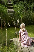 Blonde girl fishing from wooden jetty next to garden pond