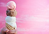 A hand holding a cone of vanilla, chocolate and strawberry ice cream