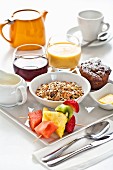 A breakfast tray with muesli, fruit, a muffin, juice and tea