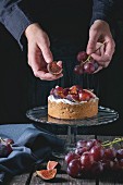 A woman's hands decorating a homemade tart with red grapes, figs and whipped cream