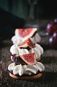 Mini cakes with sliced figs and whipped cream on an old wooden table