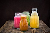 Four different smoothies in jars on a wooden table against a black background