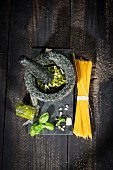 An arrangement of spaghetti, pesto alla genovese in a mortar with pesto ingredients
