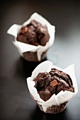 Two chocolate fudge muffins in white paper