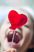 A heart-shaped lolly with a woman in the background with her mouth wide open