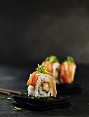 Sushi-Röllchen und Algen-Deko auf kleinen Schieferplatten