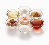 Natürliche Süssmittel im Uhrzeigersinn: Oben Stevia, Rohrzucker, Ahornsirup, Rübenzucker, Kokosblütenzucker, Agavensirup, Honig