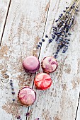 Colourful macaroons next to lavender flowers on a wooden surface (seen from above)