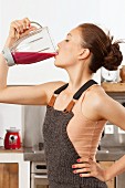 Young woman wearing pink top and dungarees drinking red smoothie from mixer