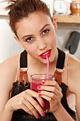 Young woman wearing top and dungarees drinking red smoothie