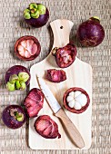 Fresh mangosteens, whole and opened with a knife on a wooden board (seen from above)